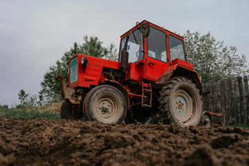Obraz premium A red tractor stands on a plowed field of dark brown color | KOROVYAKOVA, SVERDLOVSKAYA OBLAST - 9 MAY 2020.