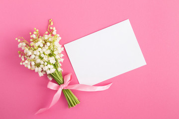 Blank white sheet of paper and bouquet of lilies of the valley on the pink  background. Top view. Copy space.