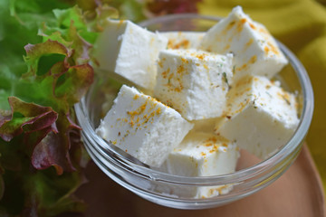 Pickled cheese with spices in a glass plate.Lettuce leaves on the table.