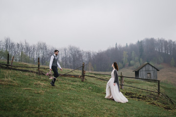 Fototapeta premium Romantic, young and happy caucasian couple in wedding clothes hugging on the background of beautiful mountains. Love, relationships, romance, happiness concept. Bride and groom traveling together.