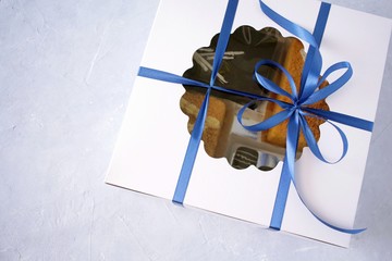 White gift box with cake and blue tape decoration on light background.
