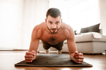 Closeup portrait of a young athlete. A young man with a sports figure has a workout at home. The brunette is looking at the camera. Stay home and keep fit