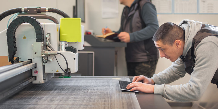 Two printshop worker technicians works on large CNC computer numerical control printing and cutting machine