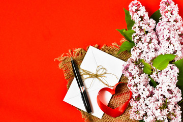 Lilac bouquet and letter with pen on a red background. Holiday card. Holiday concept. Place for text.