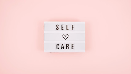 Self-care word on lightbox and flower narcissus on pink background flat lay. Take care of yourself. - obrazy, fototapety, plakaty
