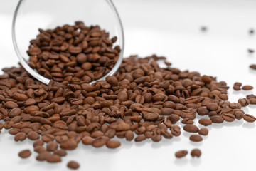 Coffee beans pour out of a glass bowl onto a light surface. coffee background