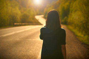 The girl goes into the sunset against the backdrop of a mountain road.
