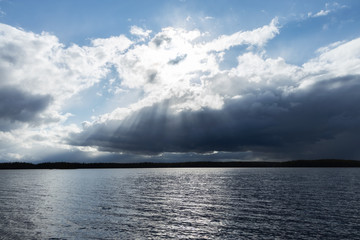 View of thunderstorm clouds above the lake. Cloudy sunset with sunbeams and blue sky.