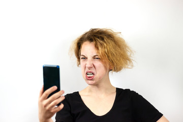 Naklejka premium A girl with yellow hair is talking via video link on a smartphone. and grimaces, Baring his teeth, a grin, on a white background. Modern technologies, youth
