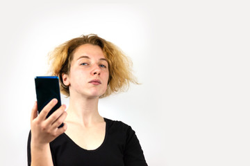 Fototapeta premium A girl with yellow hair is talking on a video link on a smartphone and looking haughtily, haughtily at the camera, on a white background. Modern technologies, youth