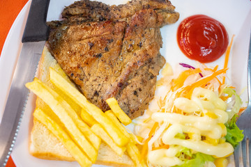 Dish of beef steak with salad, french fries and bread on red background