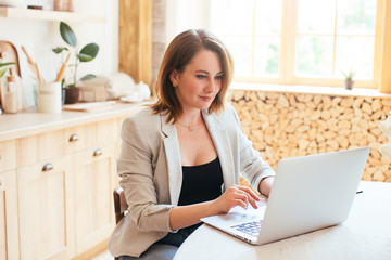 Young beautiful woman works for a computer from a home with a laptop in a kitchen as a freelancer