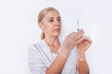 Elderly senior mature woman doctor or nurse with syringe in a white medical coat and gloves wearing personal protective equipment isolated. Healthcare and medicine concept. Covid-19 pandemic crisis