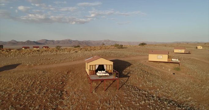 Aerial shot of lodge with empty bed in balcony against sky, drone panning over structures in resort at desert on sunny day - Namib Desert, Namibia