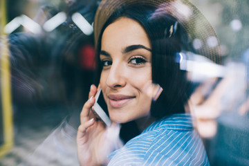 Close up portrait of beautiful female teenager looking at camera while receiving smartphone call for talking, millennial generation Y enjoying cellphone conversation during free time, soft focus