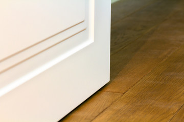 Detail of contemporary white room door on wooden yellow floor.