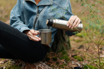 A girl drinking tea from a thermos. Tea from the thermos in the woods. Drinking from the thermos. The forest atmosphere. 