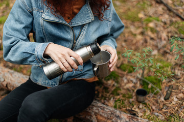 A girl drinking tea from a thermos. Tea from the thermos in the woods. Drinking from the thermos. The forest atmosphere. 