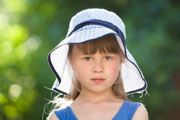 Close-up portrait of serious little girl in a big hat. Child having fun time outdoors in summer.