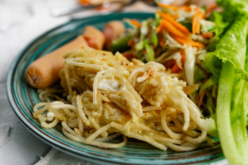 Salad of fresh vegetables on a plate with leaves, next to toasted pasta spaghetti with egg and meat sausage, a Hearty lunch, everyday productsfor a home dinner