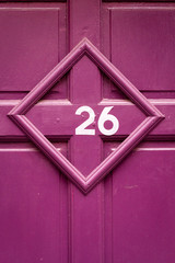 House number 26 on a purple wooden front door in a crooked picture frame
