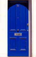 House number 51 on a royal blue wooden front door with vertical lines in London with white frame...