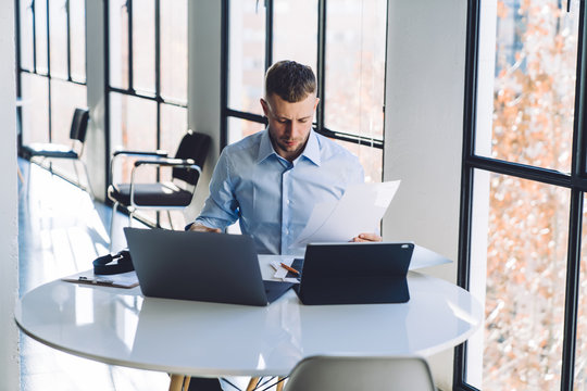Concentrated businessman revising documents while using laptops