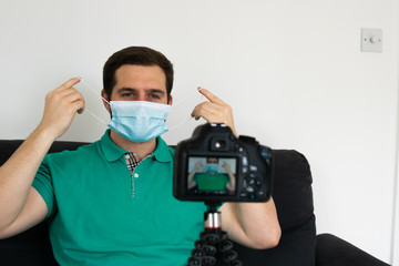 Fototapeta na wymiar Photo of a young and attractive man recording a video showing how to put a face mask.