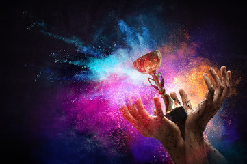 Hand holding up a gold trophy cup against dark background