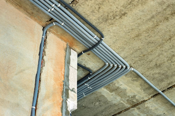 Obraz premium Electrical cables laid in protective corrugation installed on the ceiling and wall in a room under construction works.