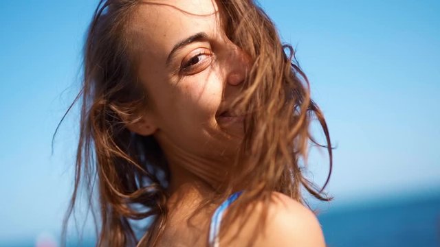 super slow motion Close Up attractive smiling woman with flying hair over face. girl face on blue sky background, wind blowing hair summertime
