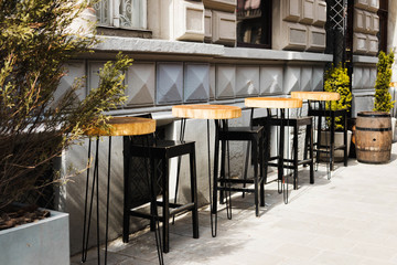 High wooden tables and chairs near the cafe, a tree in pots, old barrels,