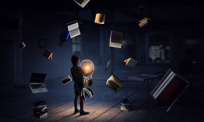Boy holding a light bulb with books around him