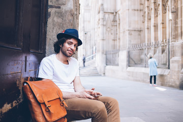 Adult relaxed traveler with smartphone smiling at camera on street in old town