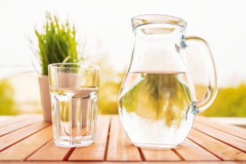 jug with water and a glass on a wooden table on the nature in the garden