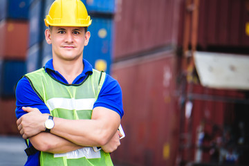 Young confident Caucasian man engineer using digital tablet and wearing yellow safety helmet and check for control loading containers box from Cargo freight ship for import and export, transport.