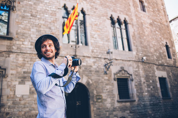 Fototapeta na wymiar Cheerful male traveler with photo camera standing on old square