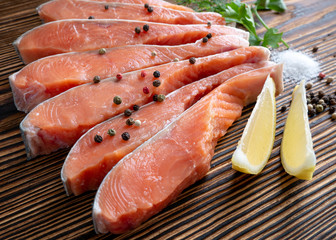 Raw red fish fillet with lemon, spices, sea salt, pepper, parsley and dill on a wooden background.
