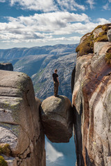 A guy standing on the famous boulder (Kjeragbolten) stuck between two rocks above a fjord. Popular...
