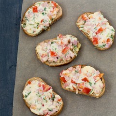 Five sandwiches are on a brown parchment paper, on a gray wooden table.