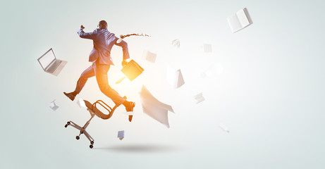 back view of running black businessman with briefcase and falling around office objects