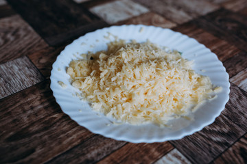 grated cheese on a grater in a white beautiful plate on a dark background