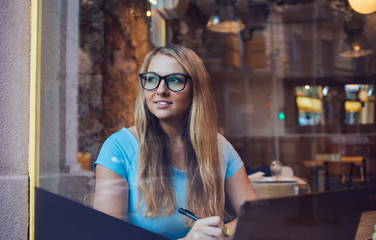 Thoughtful Caucasian writer creating idea for plot enjoying remote work in coffee shop, pondering woman in optical spectacles for eyes correction sitting at cafeteria table with modern laptop computer