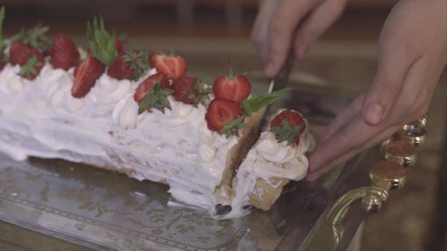 Hands of unrecognizable woman cutting freshly baked sweet strawberry Long-Cake Roll, also called Strawberry roulade