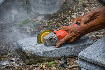 A construction worker is cutting a block brick with electric power saw holding it tight with two heavy duty hands © min