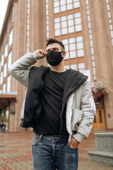 Brunette guy in a black tracksuit puts on a face mask. Black stylish face mask during a pandemic virus crown. Handmade cotton face mask for protection against viruses and bacteria.