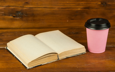 Disposable coffee cup with open book on wood table
