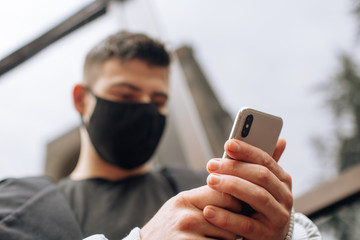 Brunette in a black T-shirt in a black face mask. Talking on the phone. Black stylish face mask during the pandemic corona virus. Handmade cotton face mask to protect against viruses and bacteria.