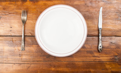 empty plate with knife and fork on empty wooden table.