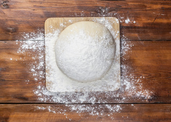 Ball of pizza dough on a rustic wooden background with dusting of flour